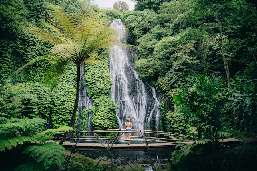 Woman standing on bridge with Banyumala Waterfall in background – Bali Waterfall Tour