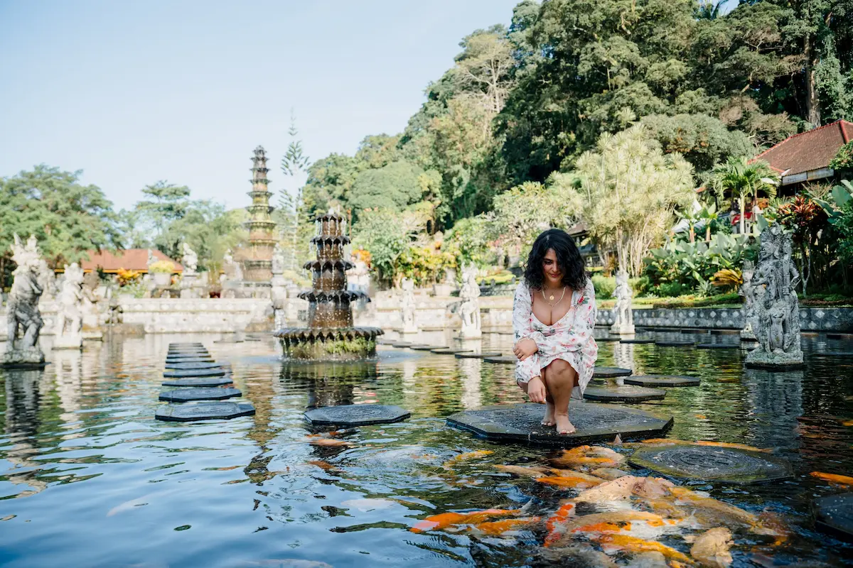 Female traveler taking photo at Tirta Gangga water palace with koi fish – one of the best Bali Instagram spots.