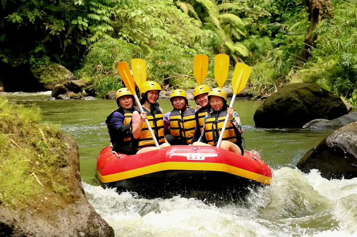 Guests enjoying white water rafting tour in Bali, paddling through rapids surrounded by jungle scenery.